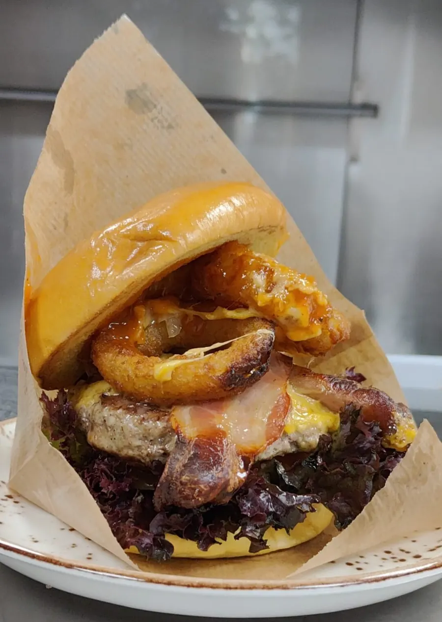 Burger mit Zwiebelringen und geschmolzenem Käse, in Papier serviert