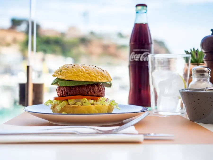 Veganer Rote-Bete-Burger auf der Terrasse, im Hintergrund die Boote des Hafens